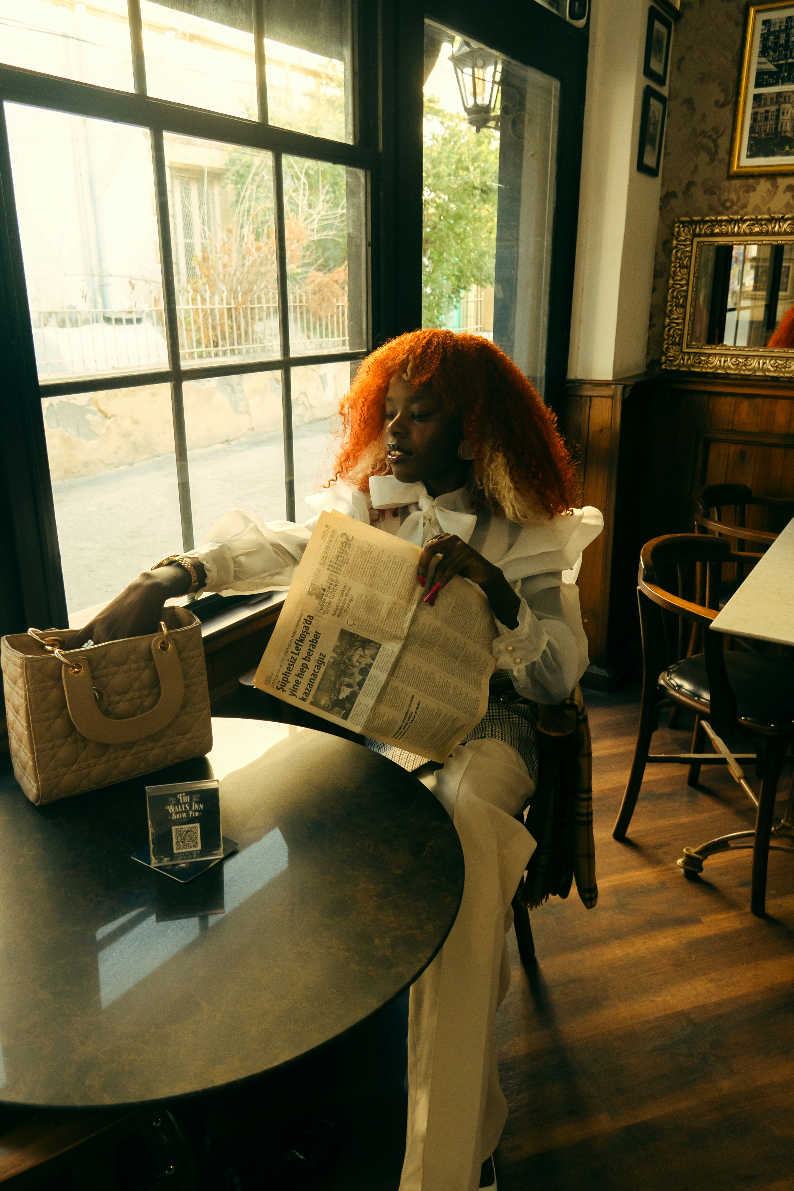 A woman reading a newspaper beside a café window.