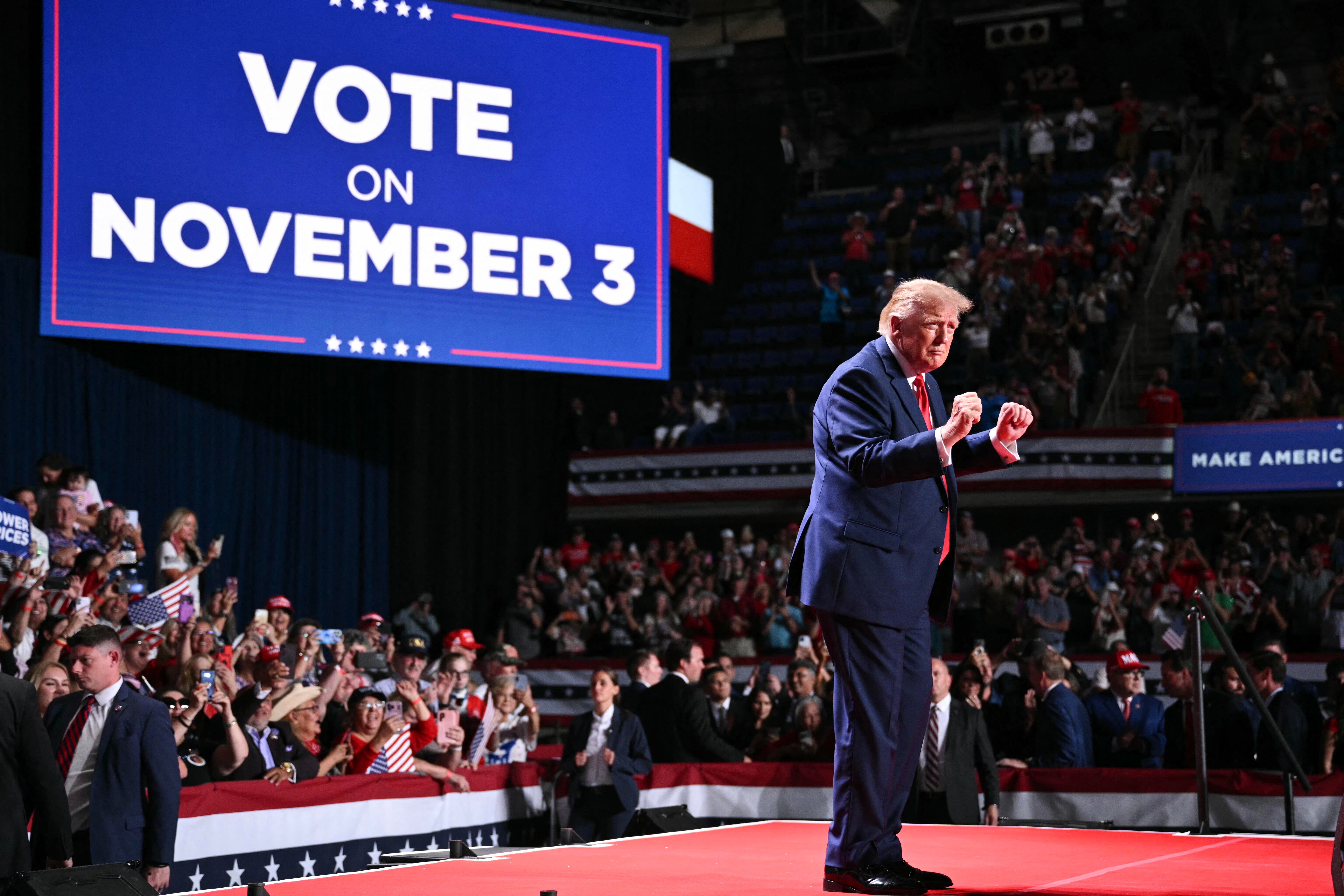 Donald Trump on a rally stage beside a sign reading Vote on November 3.