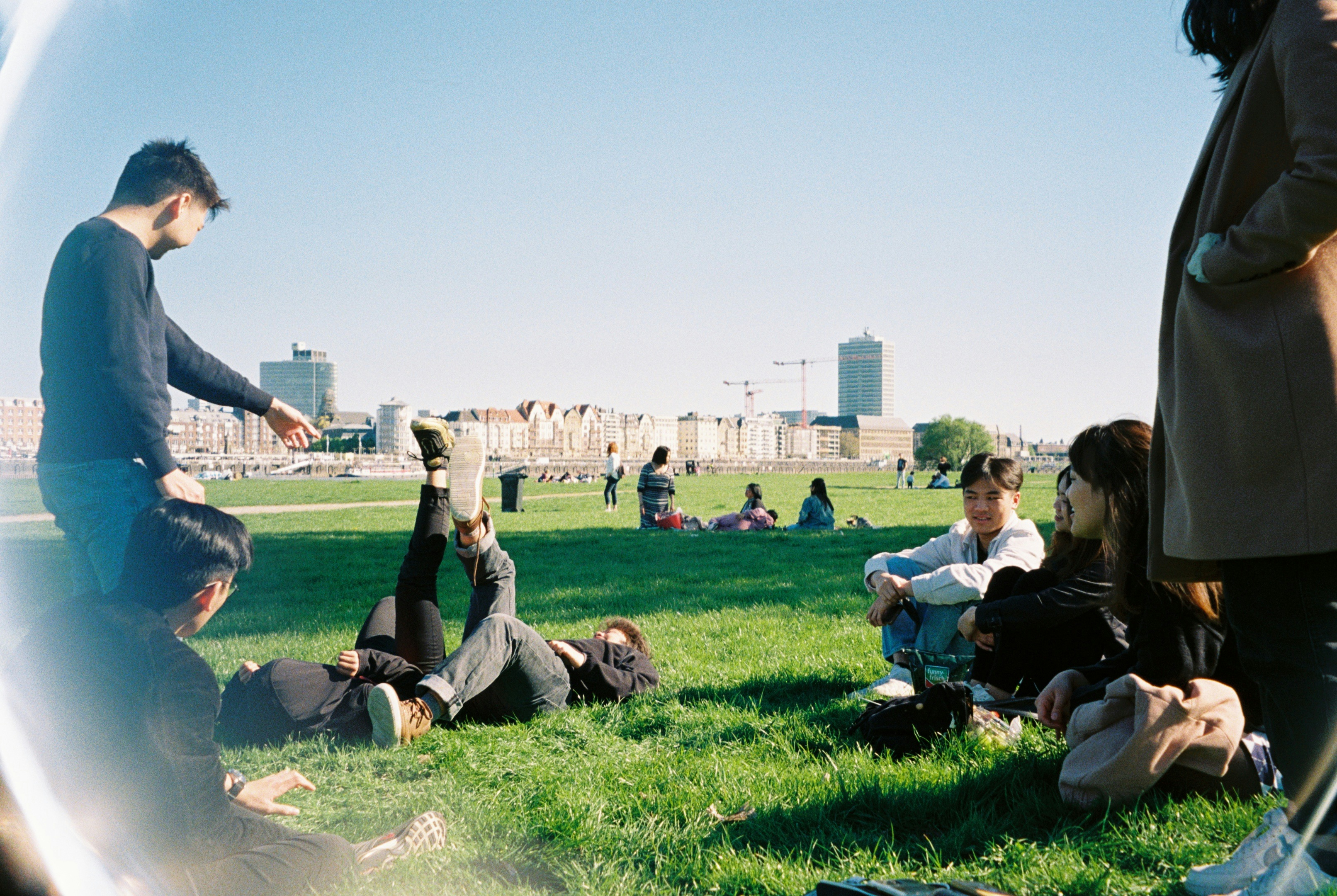 Young friends sitting and lying on the grass together in a sunny city park.